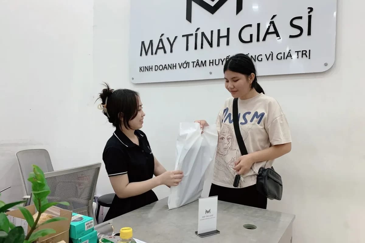 Nhân viên MTGS giao máy cho khách tại quầy, dưới bảng hiệu cửa hàng